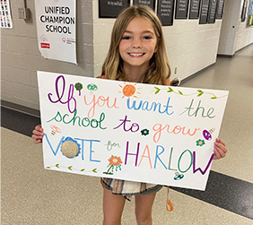 Girl holding sign that reads, if you want the school to grow vote for Harlow