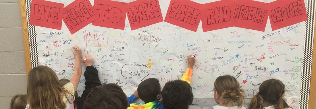 Students signing - we pledge to make safe and healthy choices board